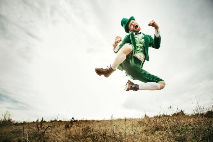 सेंट पैट्रिक डे के लिए पूरी तरह से तैयार एक रूढ़िवादी आयरिश चरित्र आयरिश देश के एक खुले मैदान में कूदता है और नृत्य करता है आकाश और घास में कॉपी स्पेस