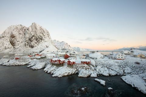 Lofoten द्वीप Hamnoy नॉर्वे में पहाड़ी दृश्य के साथ बर्फ के बीच लाल मछली पकड़ने के घर गांव